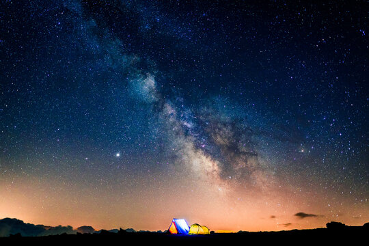 Tents glowing under the milky way at night. Camping in the mountains under the starry magical sky. 5 Billion Star Hotel.
