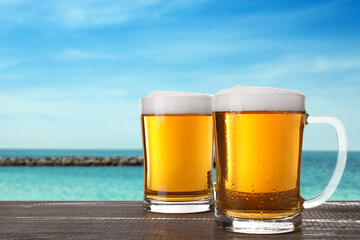 Cold beer on wooden desk against blurred sea. Space for text