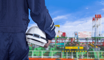 Close up engineer hand in blue mechanic jumpsuit holding white safety helmet with blurred crude oil...