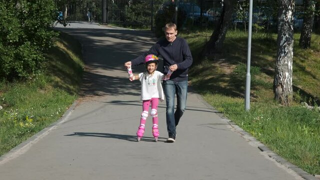 Father Teaching his Little Daughter Inline Skating in a City Park. Childhood, Summer Activities and Healthy Lifestyle Concept