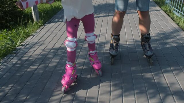 Closeup of Little Girl Learning Roller Skating with her Mother in a City Park. Slow Motion. Summer Family Activities and Healthy Lifestyle Concept