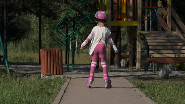 Cute Little Girl Wearing Protection Pads and Helmet Roller Skating near a Playground. Slow Motion. Childhood, Summer Activities and Healthy Lifestyle Concept