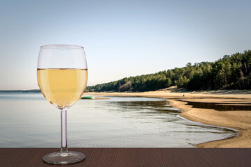 Glass of white wine with view of the White Dune and Baltic see in spring, Latvia. Beach with white sand and blue sea/ocean. Beach with pine forest