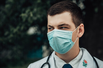 Close up portrait of young doctor wear medical gown, face mask and stethoscope. Protection from epidemic disease. Man want to be healthy. Coronavirus concept. Confident profession.