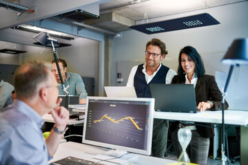 Smiling mature female and male colleagues discussing over graph while planning strategy at workplace