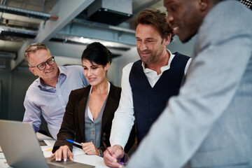 Confident mature businesswoman planning strategy with male colleagues while using laptop at office...