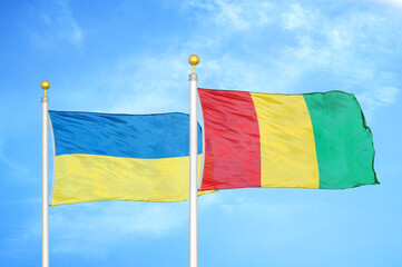Ukraine and Guinea two flags on flagpoles and blue sky