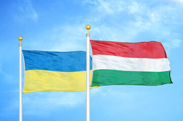 Ukraine and Hungary two flags on flagpoles and blue sky