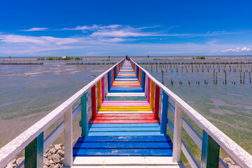 Fototapeta premium Rainbow bridge in Thailand.View of The colorful wood bridge extends into the sea under blue sky at samut sakhon province,Thailand.