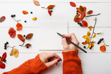 Top view mock up woman hands with notebook on wthite wooden background with autumn leaves. 'To do'...