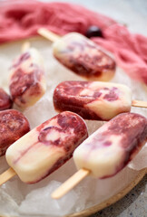 Fresh cream and cherry homemade popsicles placed on white ceramic plate with fruits and textile
