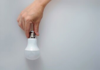 man's hand holds energy saving light bulb on gray background