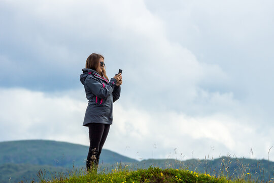 Girl with cell phone in her hand are standing on a hill ltaking a picture with smart phone. Tourist, technology and travelling concept.