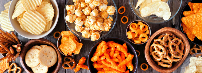 Variation of salty snacks. Overhead view table scene on a dark wood banner background.