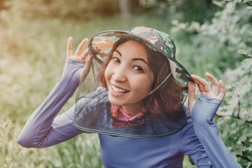 Happy girl in a hat with an anti-mosquito net in the forest. Protection from blood sucking insects carriers of pathogens and diseases