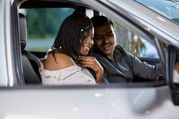A beautiful couple smiles inside a car interior in a car dealership looking at a car, selective focus
