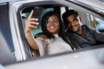 A beautiful couple smiles inside a car interior at a car dealership taking selfies, selective focus