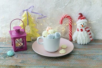 Merry Christmas, a cup of coffee with meringues and caramel, a lantern with a burning candle, festive decor, wooden light background, the concept of home comfort, congratulations on the winter holiday