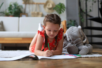 Smilling happy girl lying on warm floor with a toy elephant near to her enjoying creative activity,...