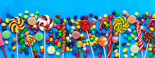 Border colorful lollipops and colored round candies on a blue background. Festive sweet background. Top view, flat lay.