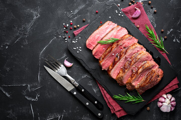 Juicy delicious grilled beef steak medium rare cut into pieces on a slate plate, black stone...