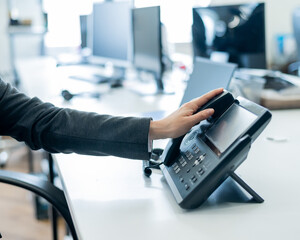Closeup female hand on landline phone in office. Faceless woman in a suit works as a receptionist answering the phone to customer calls.