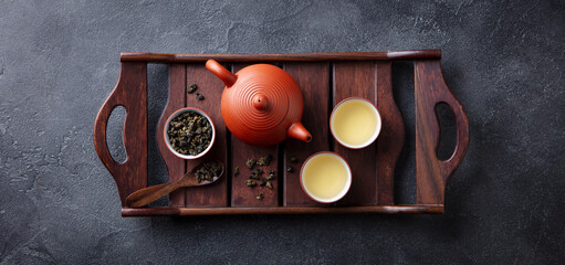 Green tea oolong in teapot and chawan bowls, cups on a wooden tray. Grey background. Top view.