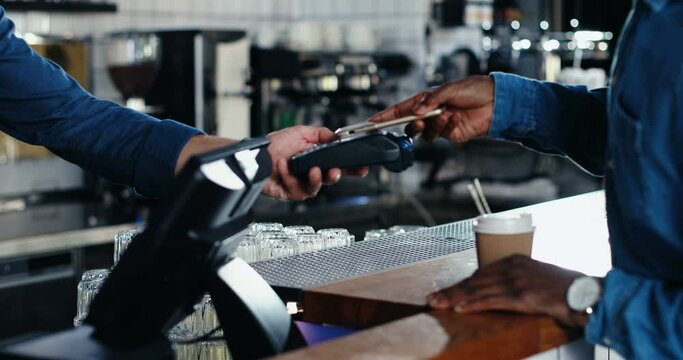 Close up of hands of multiethnic bartender and client men. African American male client paying with paypass on credit card. Mixed-races. Passing payment at counter. Pay for drink or food in cafe.