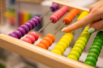 Closeup female hand calculating with balls on wooden rainbow abacus for number calculation. The concept of learning arithmetic for preschoolers.