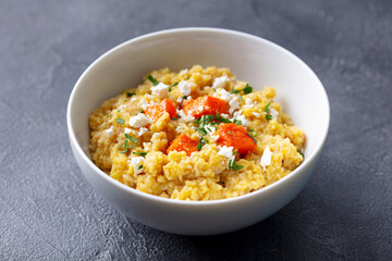 Spelt porridge with roasted pumpkin and cream cheese in bowl. Grey background. Close up.