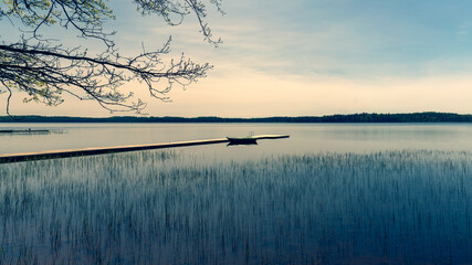 Walk by the lake among the trees on a sunny spring day. Boats with oars moored to the shore. The girl on the pier enjoys calm. Latvia