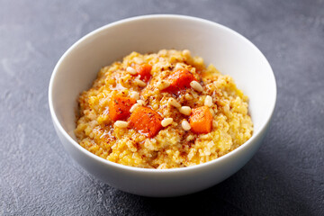 Spelt porridge with roasted pumpkin and pine nuts in bowl. Grey background. Close up.