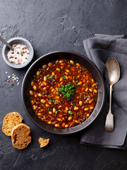 Bean soup in a black bowl. Grey background. Close up. Top view.