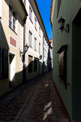 Fototapeta na wymiar Narrow street in the old town of Riga. Blue sky between the facades of old houses with lamps.