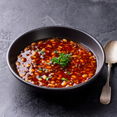 Bean soup in a black bowl. Grey background. Close up.