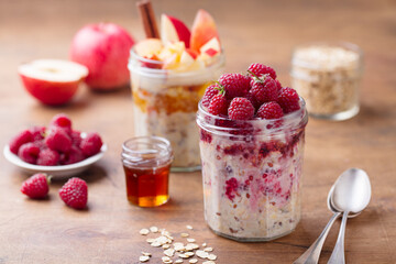 Overnight oats, bircher muesli with raspberry and apple in glass jars. Wooden background. Close up.
