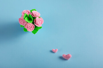 The pot of handmade felt pink roses on a blue background with pink hearts. Copy space. Holiday card, congratulation, invitation. Top view