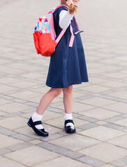 A girl in a school uniform with a backpack on her back stands with her back to the camera