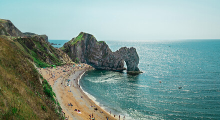 Durdle Door, Jurassic Coast near Lulworth in Dorset, England - a natural limestone arch. Durdle Door with people relaxing on the beach on a sunny day in August 2020.