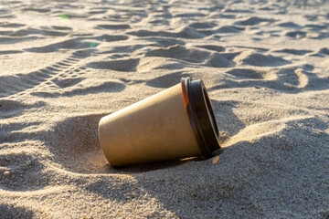 Disposable coffee cup on the beach. Nature protection and pollution concept.  - obrazy, fototapety, plakaty