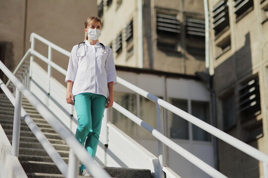 Female Doctor Or Nurse In A Protective Face Mask Walking Up The Stairs