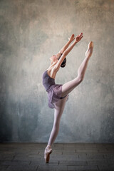 graceful ballet dancer in a light lilac suit and pointe shoes against a gray wall. Dance, grace, artist, contemporary, movement, action and freedom of movement concept.