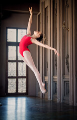 young ballerina in a red leotard froze in a jump in a luxurious interior