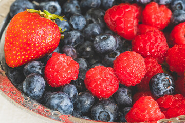 Fresh ripe washed strawberries, blueberries, raspberries in colander close up on white background