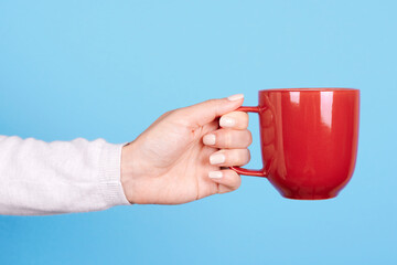 Hand with red mug with handle. Isolated on blue background.