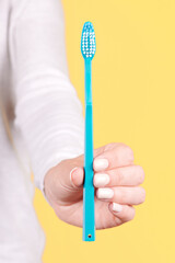 Hand with blue toothbrush, dental care. Isolated on yellow background.
