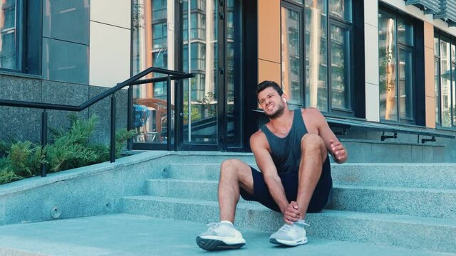 Young man exercising outside. Guy running or jogging on street. Suddenly hurt or injure his leg or ankle. Suffer from pain and scream because of it. Sporty trauma.