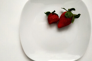 Two strawberries on a plate, one strawberry bitten, close-up, berry on a white glossy plate, place for an inscription.
