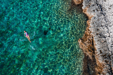 Top aerial view of the young female floating on the back and relaxing on the warm turquoise...