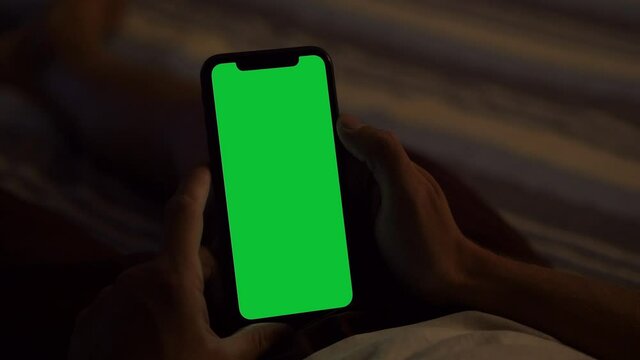 Milan, Italy - August 202: Holding a Green Screen iPhone, Lying on the Bed at Dusk